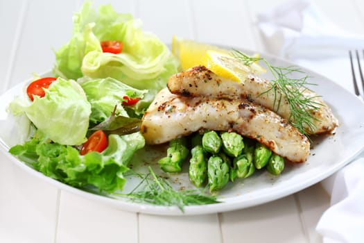Delicious fried fish on green asparagus with salad