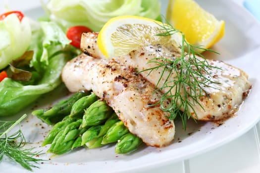 Delicious fried fish on green asparagus with salad