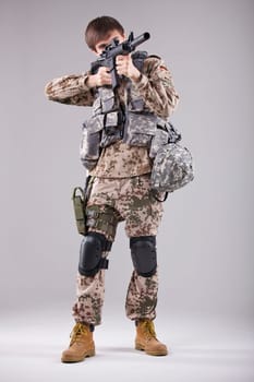 Soldier in camouflage aiming with machine gun in a white studio