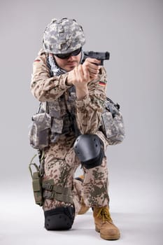 Soldier in camouflage aiming with gun in a white studio