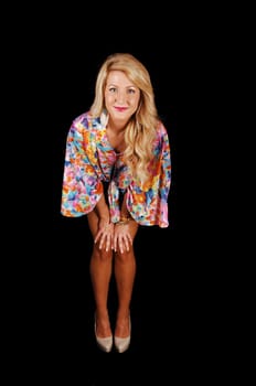 A lovely young blond woman standing in the studio for black background with her hands on her knee and bending forwards.