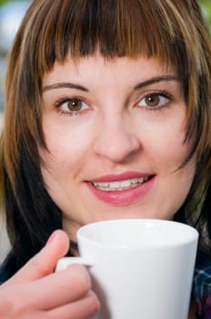 Close-up of a brown-haired young woman holding a white cup in a street café