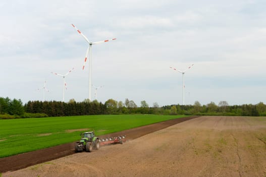 farmer plowing a field with several windmills in the background