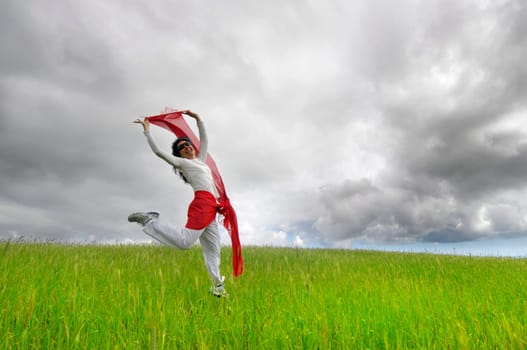 Woman jumping high in a green field with a scarf
