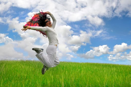 Woman jumping high in a green field with a scarf