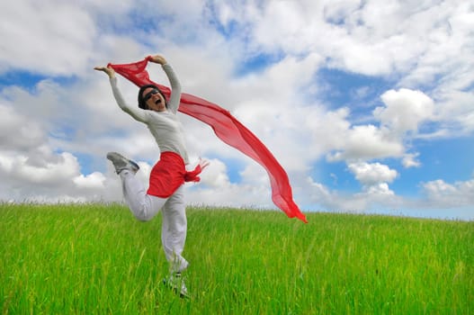 Woman jumping high in a green field with a scarf