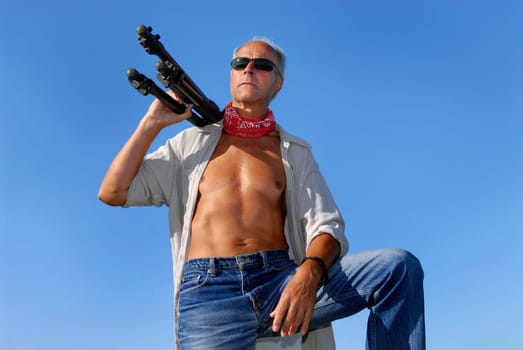 Handsome mature man adventurer, posing with a tripod outdoors
