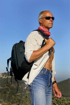Handsome mature man adventurer posing with a backpack outdoors