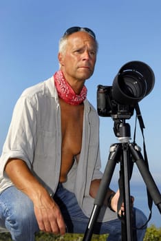 Handsome mature man posing with a big camera outdoors