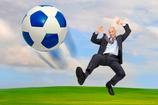 Mature businessman playing soccer outdoors in a green field