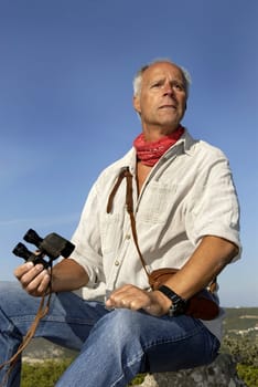 Mature man model posing outdoors with is binoculars looking for adventure