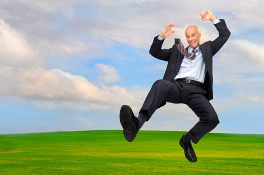Happy mature businessman jumping outdoors in a green field