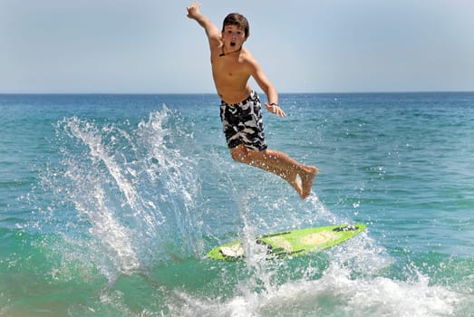 Boy jumping in the air with skimboard in the sea