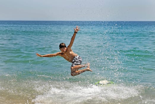 Boy jumping in the air with skimboard in the sea