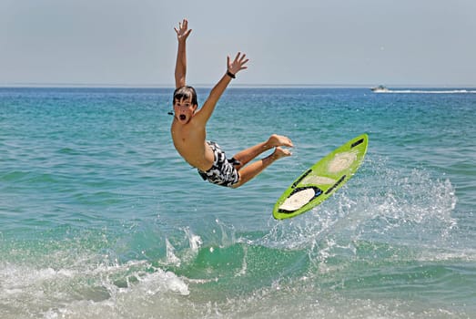 Boy jumping in the air with skimboard in the sea