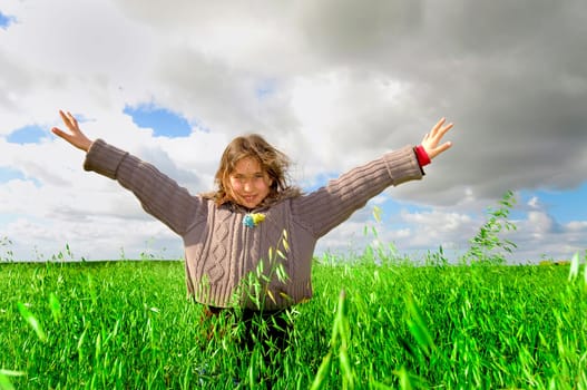 Beautiful young girl in a windy green field with open arms