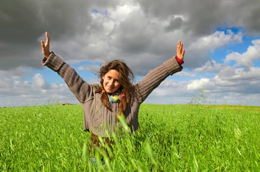 Beautiful young girl in a windy green field with open arms