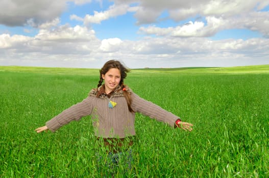 Beautiful young girl in a windy green field with open arms