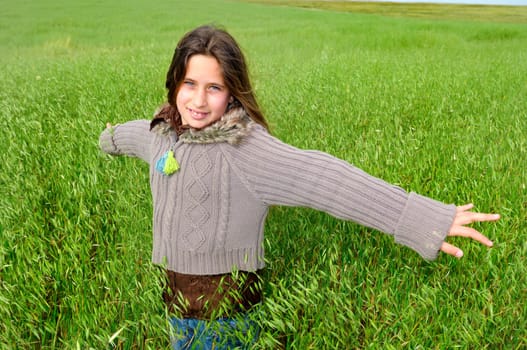 Beautiful young girl in a windy green field with open arms