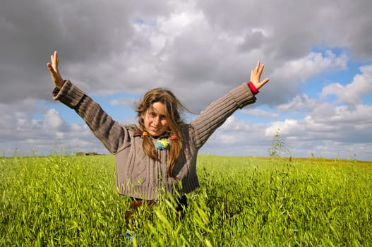 Beautiful young girl in a windy green field with open arms
