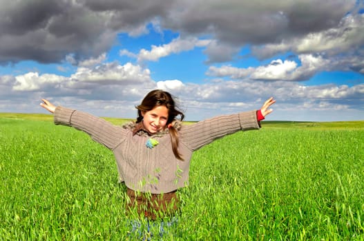 Beautiful young girl in a windy green field with open arms