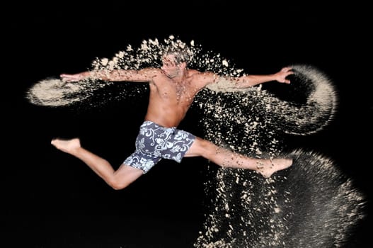 Muscular young man jumping with sand in the beach by night