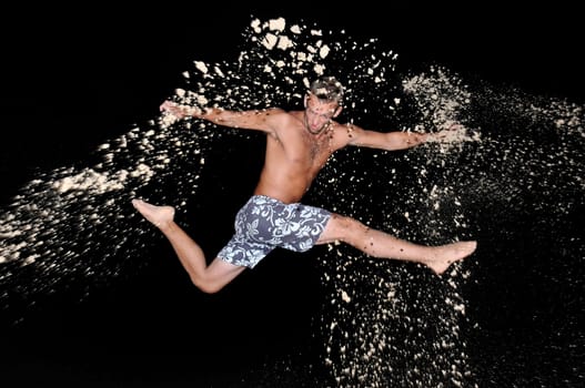 Muscular young man jumping with sand in the beach by night