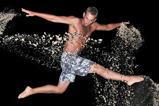 Muscular young man jumping with sand in the beach by night