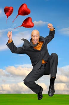 Man jumping outdoors in a green field with red heart shaped balloons