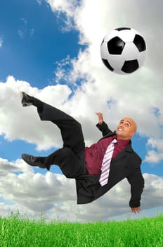 Businessman in a acrobatic pose kicking a soccer ball in a green field