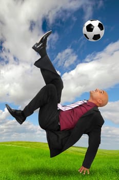 Businessman in a acrobatic pose kicking a soccer ball in a green field