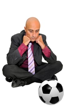 Businessman seated on the floor looking at a soccer ball, isolated in white