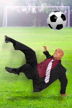 Businessman in a acrobatic pose kicking a ball in a soccer field