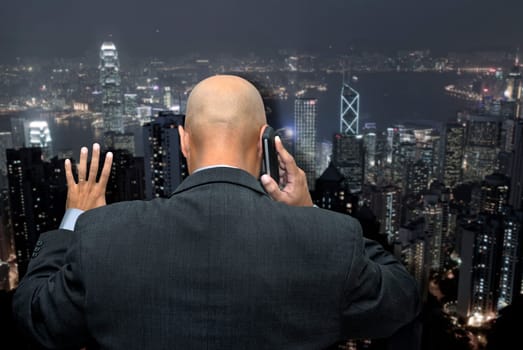 Businessman back, making a call by cellphone looking at the busy city lights, from his office
