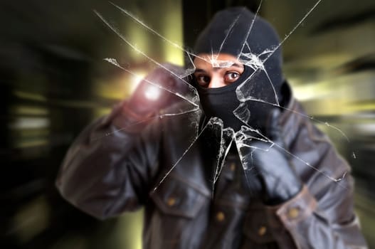 Burglar with flashlight over a broken glass