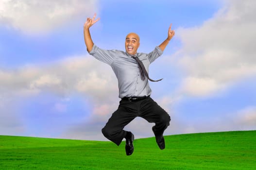 Happy businessman jumping outdoors in a green field