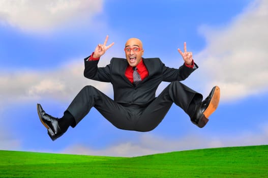 Happy businessman jumping outdoors in a green field