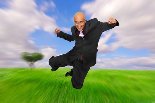Powerful and happy businessman jumping in a green field