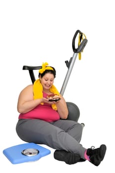 Large girl with fitness bicycle and a scale, holding a cake isolated in white