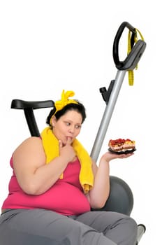 Large girl laying near a fitness bicycle looking at an irresistible cake