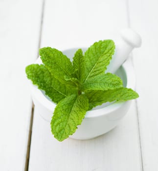 Some leaves of Mint in a mortar with pestle on a wooden table for herbs concepts