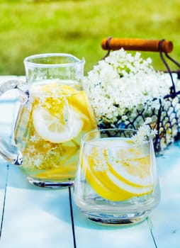 Lemon and cedar refreshment. Flowering Cedar Lemonade with water and citrus slices outdoors on a wooden table. A basket with blooming cedar in the background