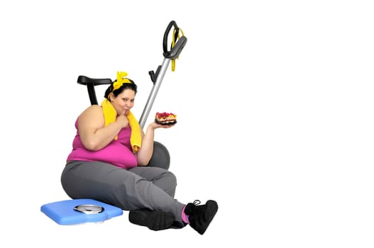 Large girl with fitness bicycle and a scale, holding a cake isolated in white
