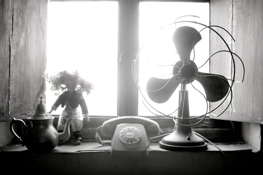 Antique vintage air fan, doll and phone at the window backlight