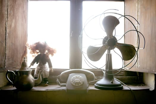 Antique vintage air fan, doll and phone at the window backlight