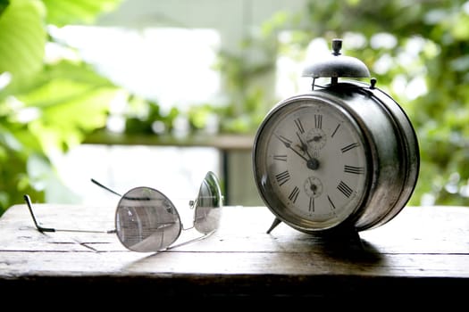 Old alarm bell clock at the window backlit in a house room with plants