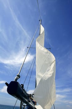 Sailor in sailboat rigging the sails over sunny summer blue sky
