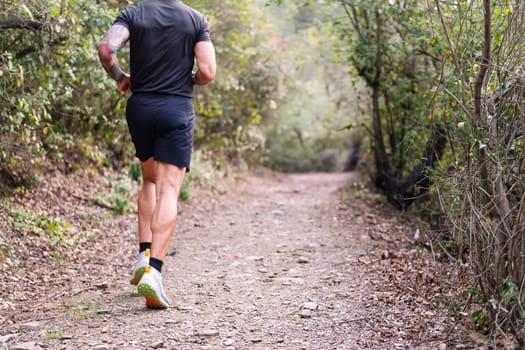 unrecognizable man practicing trail running in the forest, concept of sport in nature and healthy lifestyle, copy space for text