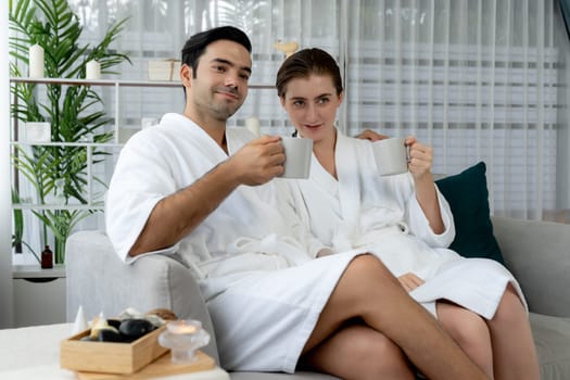 Beauty or body treatment spa salon vacation lifestyle concept with couple wearing bathrobe relaxing with drinks in luxurious hotel spa or resort room. Vacation and leisure relaxation. Quiescent