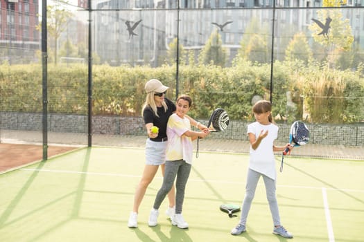 Young sporty woman with children playing padel game in court on sunny day. High quality photo